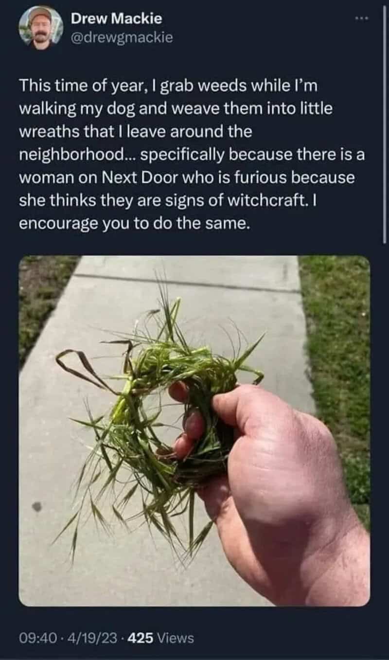 Person holding a small wreath made of weeds and grass on a sidewalk.