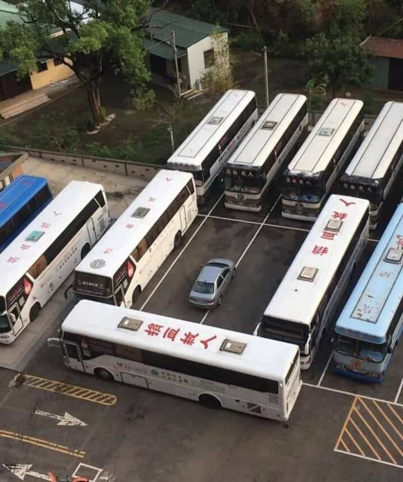 A parking lot with several buses and a small car in the center.
