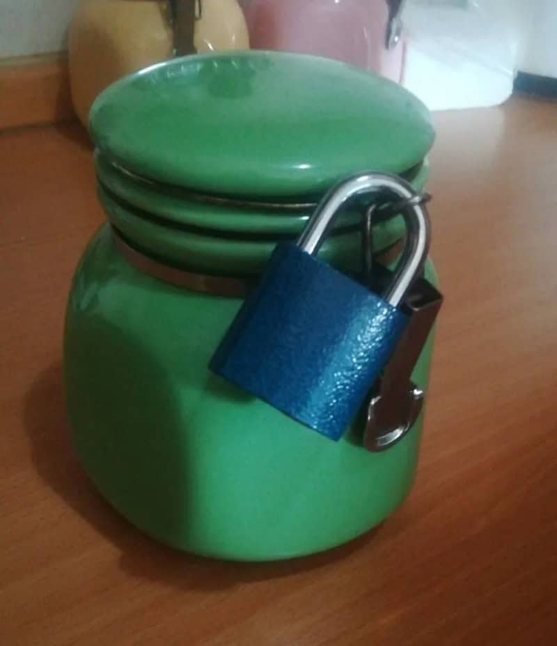 Green jar with a blue padlock attached, on a wooden surface.