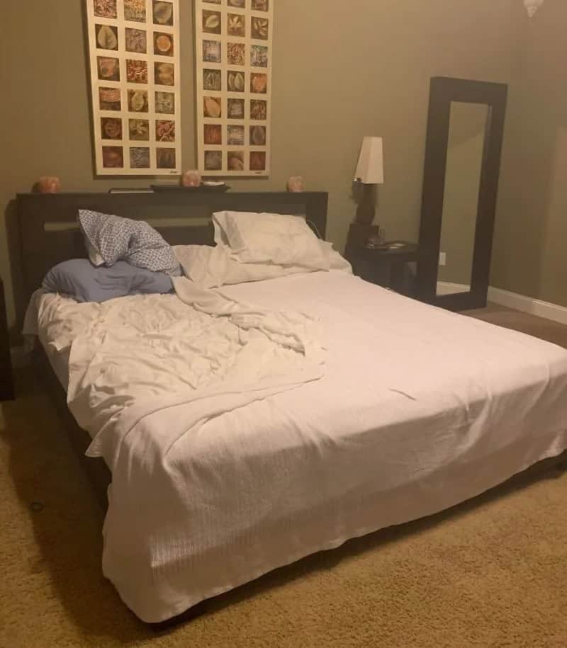 Messy bed with pillows and blankets, mirror, and wall art in the background.