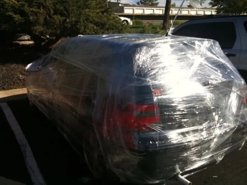 Car wrapped in plastic wrap in a parking lot.