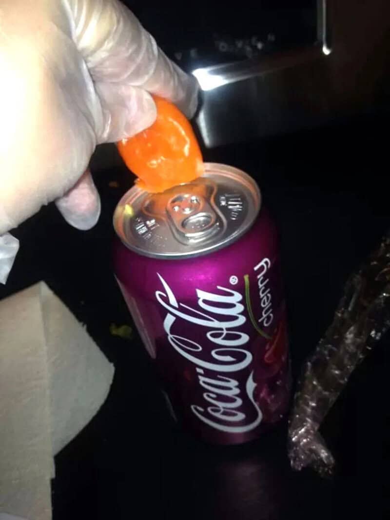 Person opening a Coca-Cola can with a plastic orange cap on top.