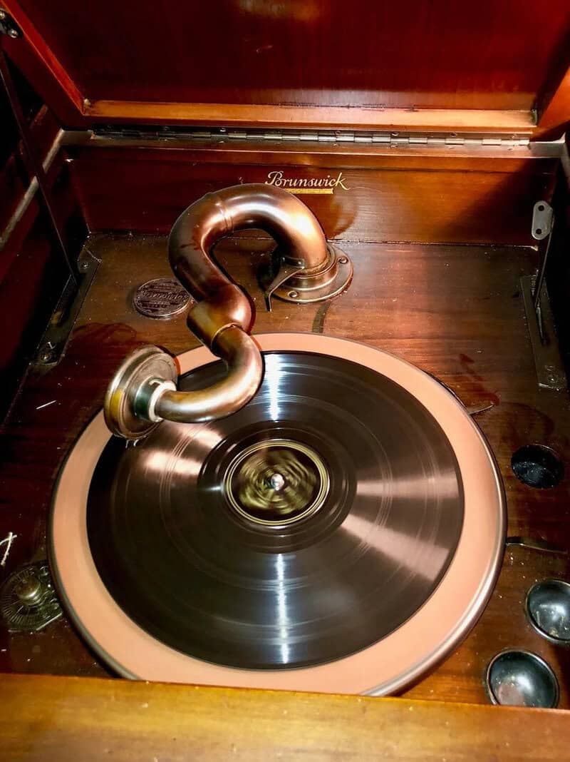 Vintage Brunswick gramophone with a spinning record inside a wooden cabinet.