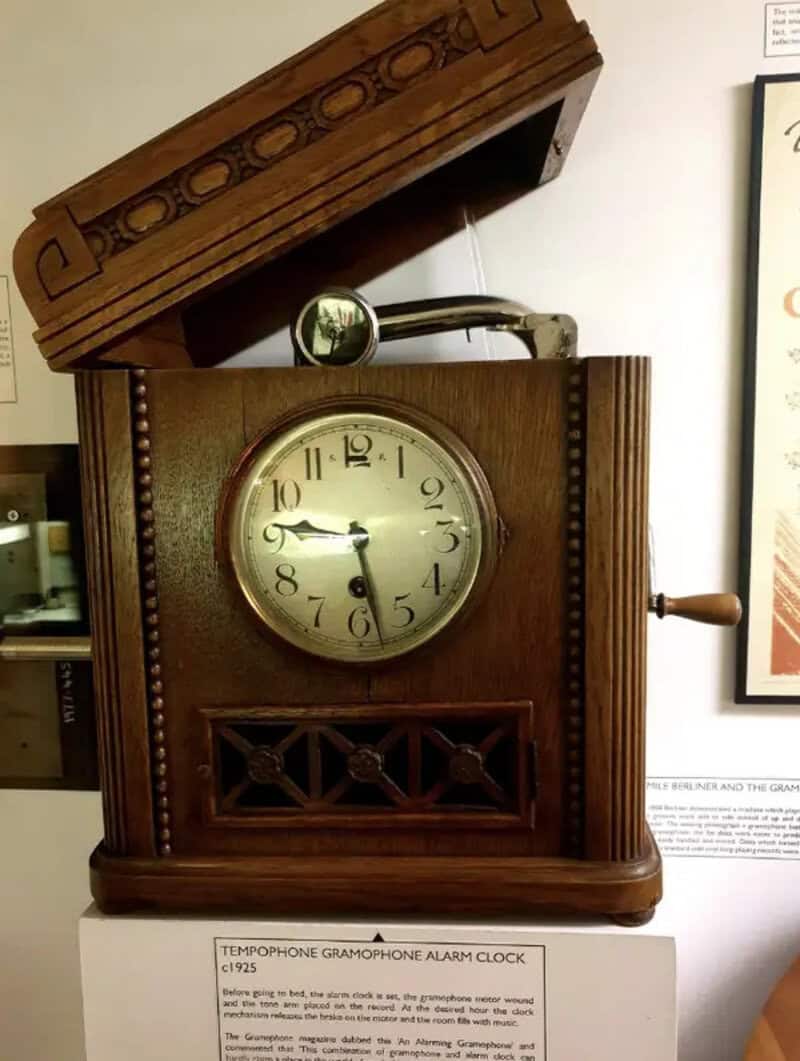 Vintage wooden gramophone alarm clock with a clock face and a lid open.