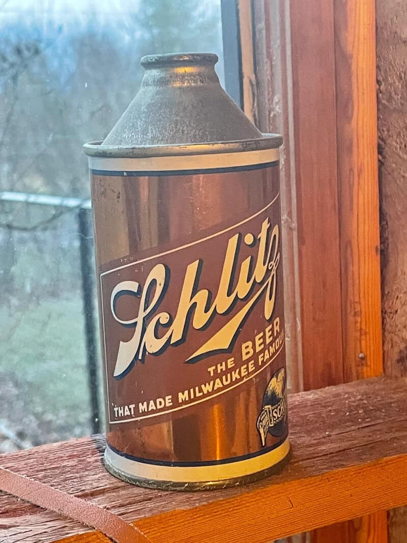 Vintage Schlitz beer can on wooden surface near window.