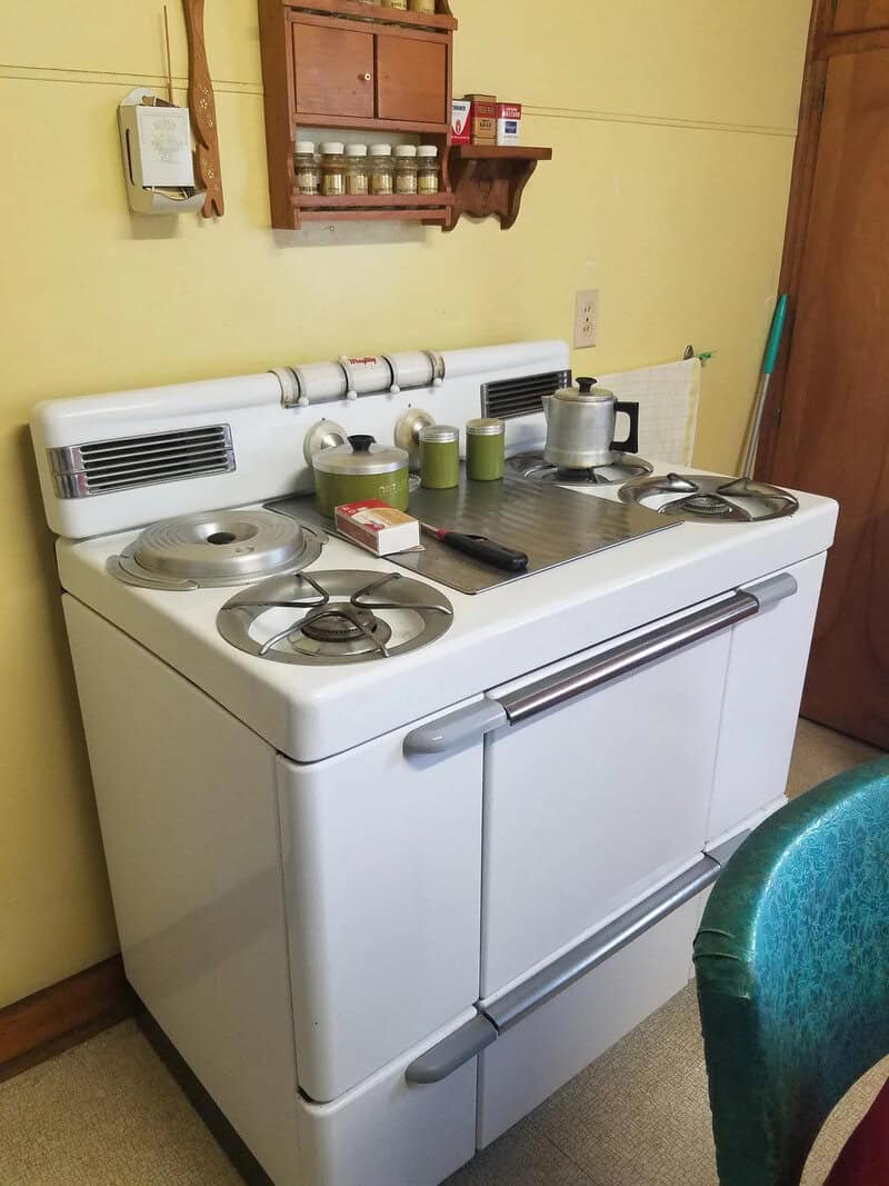 Vintage stove with kitchen items on top, in a yellow room.