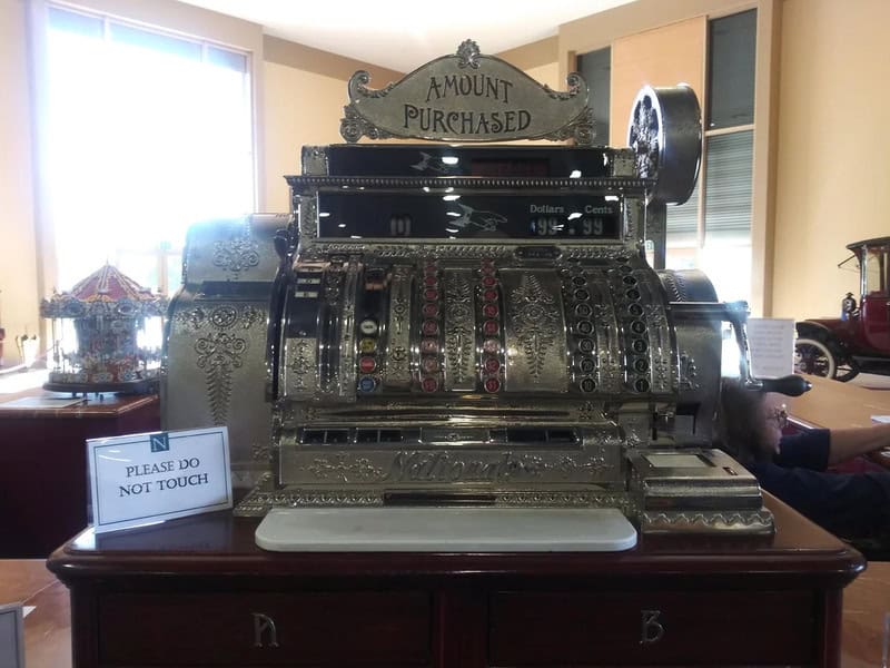 Vintage cash register with 'Amount Purchased' sign on a wooden table.