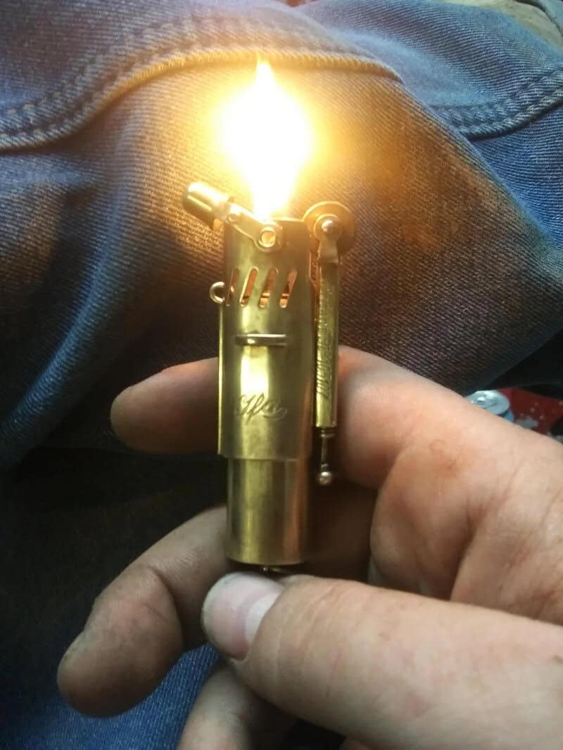 Brass lighter ignited with flame, held in hand over denim fabric.