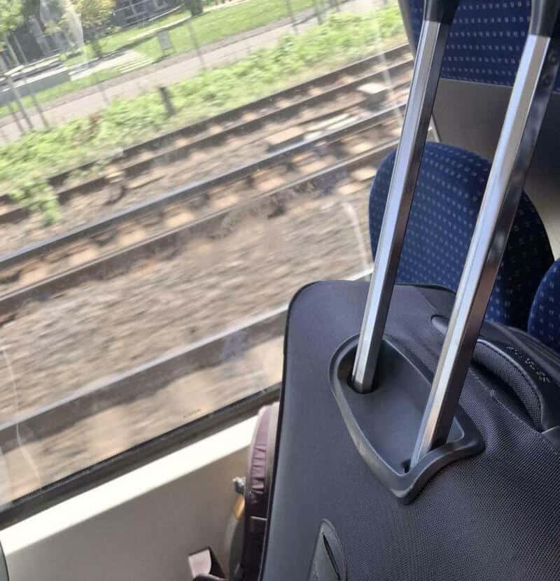 View from train window showing luggage on seat and railway tracks outside.