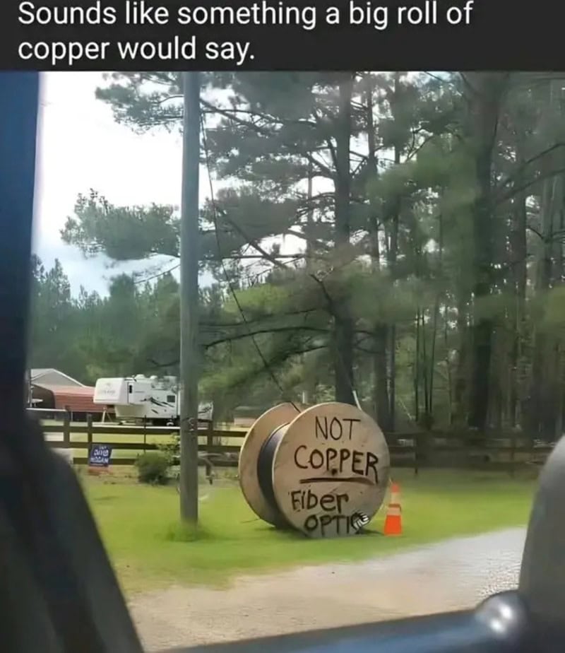 A large copper-colored fiber optic cable spool with a sign saying 'NOT COPPER' in a park.