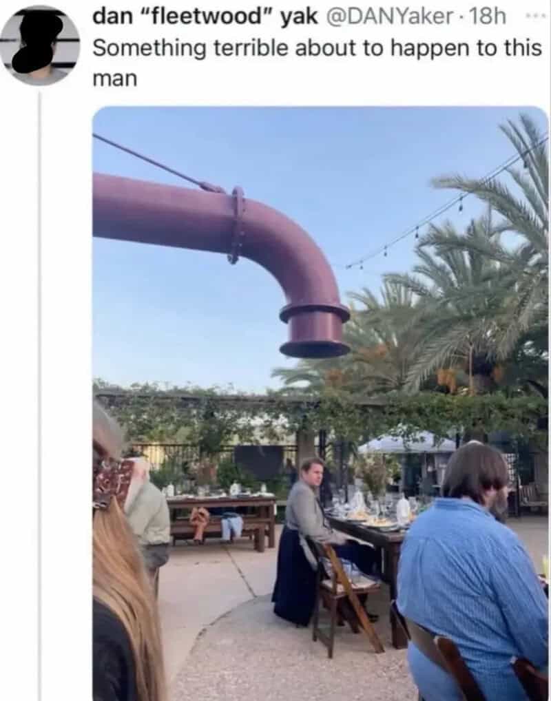 Large rusted pipe hanging above outdoor dining area with people sitting.