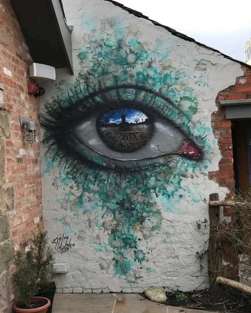 Large eye mural on brick wall with blue and green splashes.