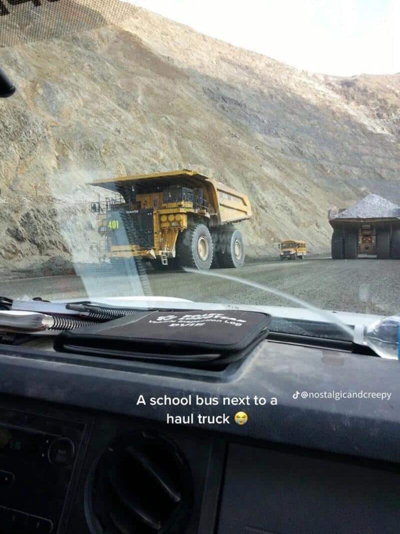 A school bus next to a haul truck on a mountain road.