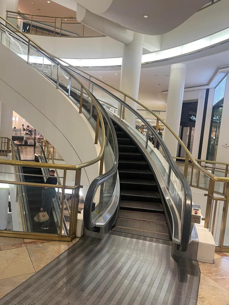 Escalator in a shopping mall with a wheelchair ramp beside it.