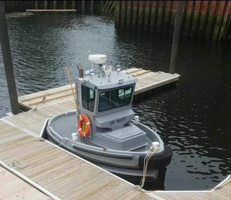 Small US Navy boat docked at a wooden pier on calm water.