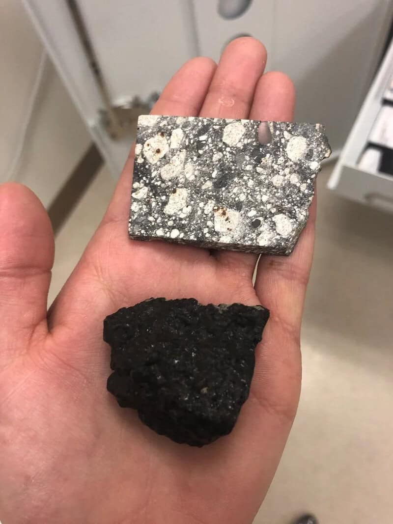 Hand holding two rocks, one with a speckled pattern and one black and rough.