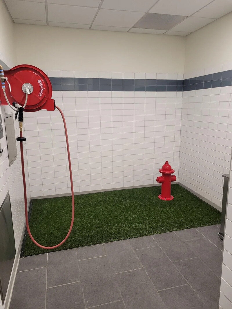 Fire hose reel and fire hydrant in a room with artificial grass and tiled walls.