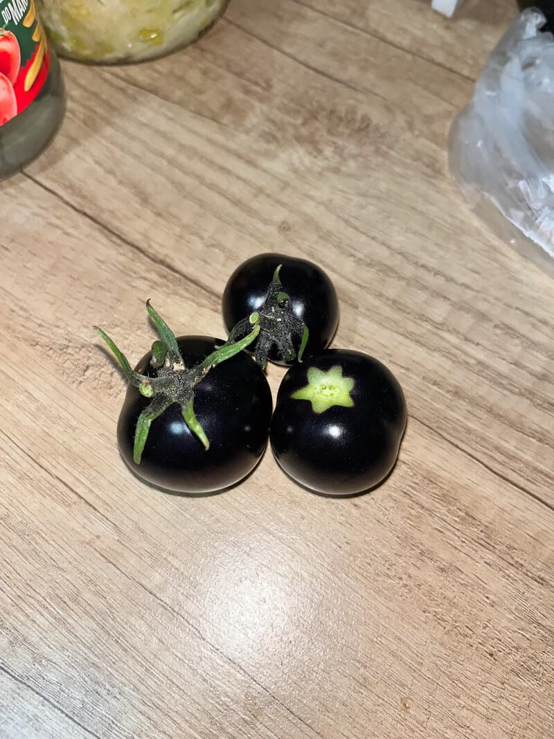 Three black tomatoes with green stems on a wooden surface.