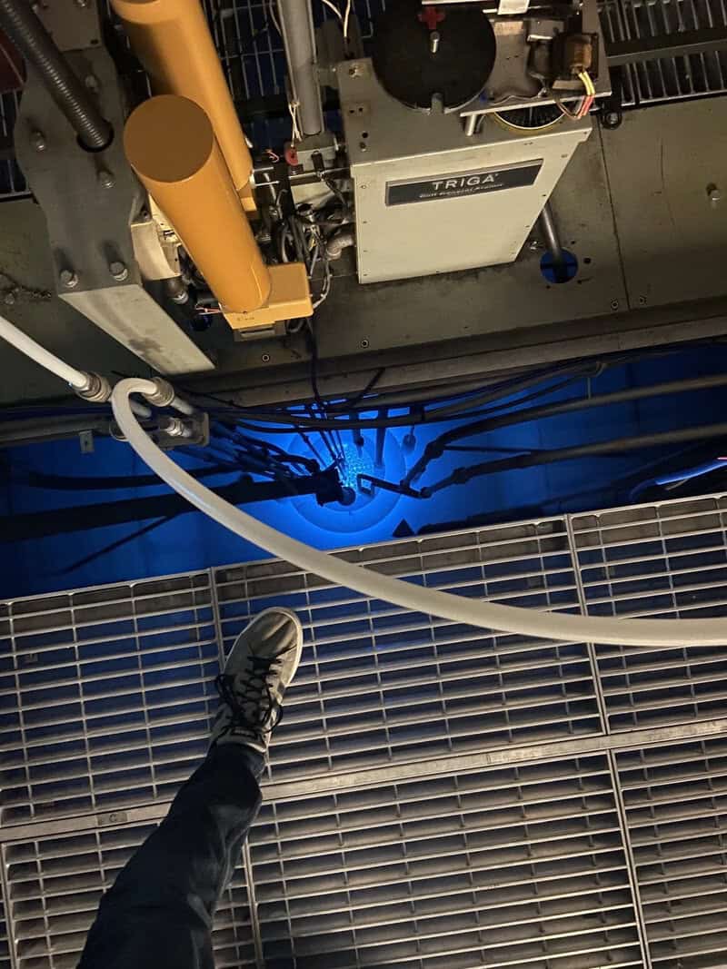 Person standing on a metal grate floor above machinery and blue-lit equipment.