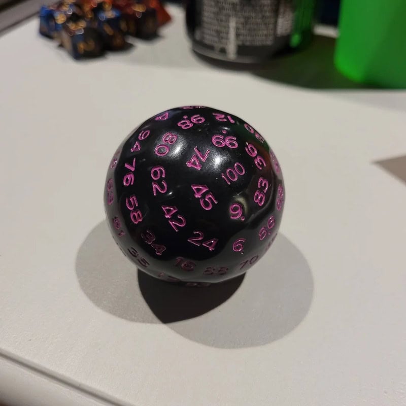 Black sphere with pink numbers and a shadow on a white surface.