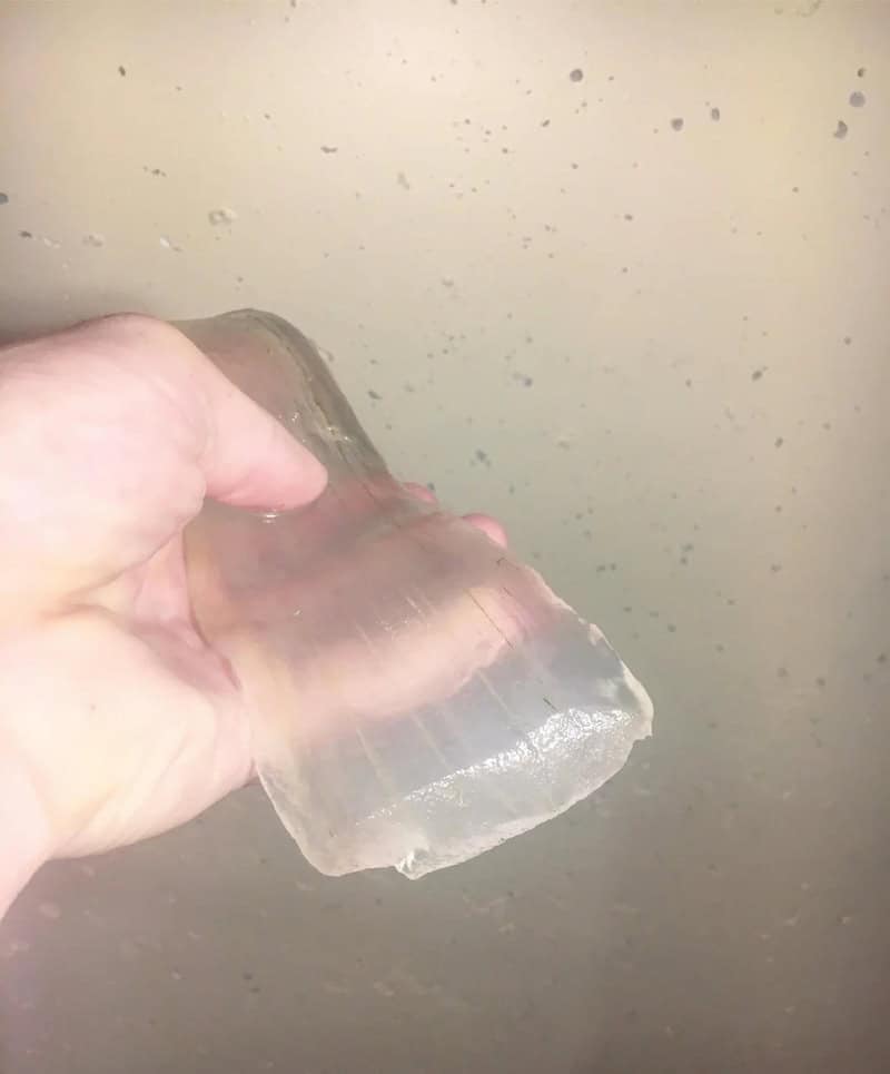 Hand holding a large, clear ice cube against a plain background.
