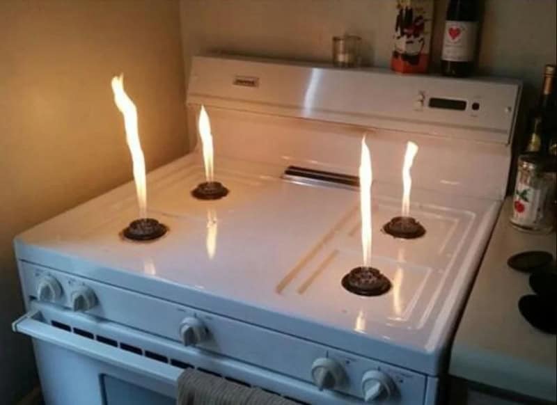 Stove with four burners, three of which are on fire, in a kitchen setting.