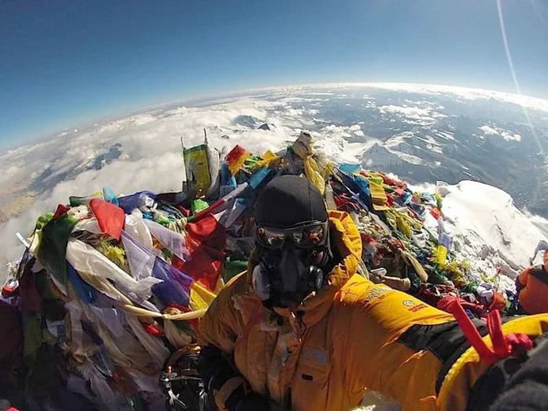 Skydiver in yellow jumpsuit with a helmet and oxygen mask, surrounded by colorful parachute fabric,.