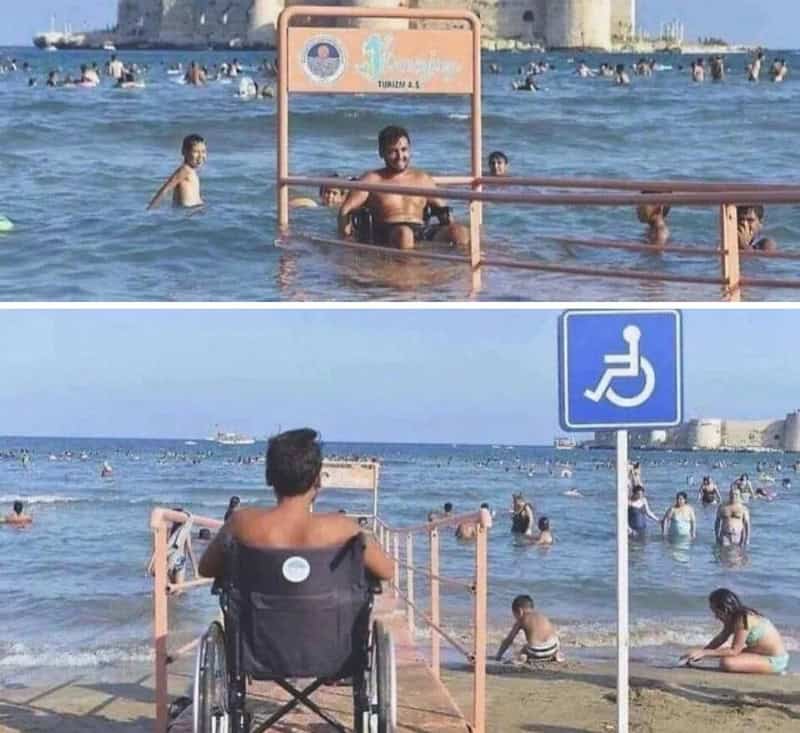 Beach scene with a man in a wheelchair and a man in the water, both near a handicap sign.