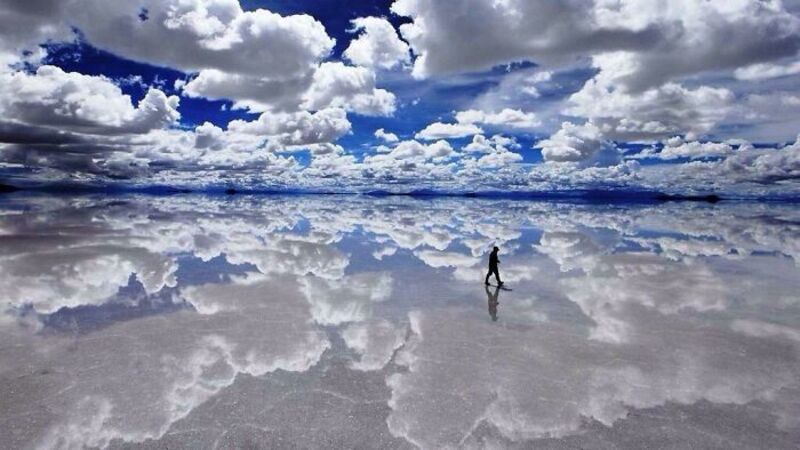 Person walking on a vast salt flat with a dramatic cloudy sky above.
