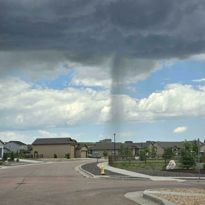 Tornado forming in the distance over a suburban neighborhood under dark storm clouds.