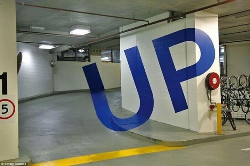 Large blue 'UP' sign in underground parking garage with bicycles and fire hose.