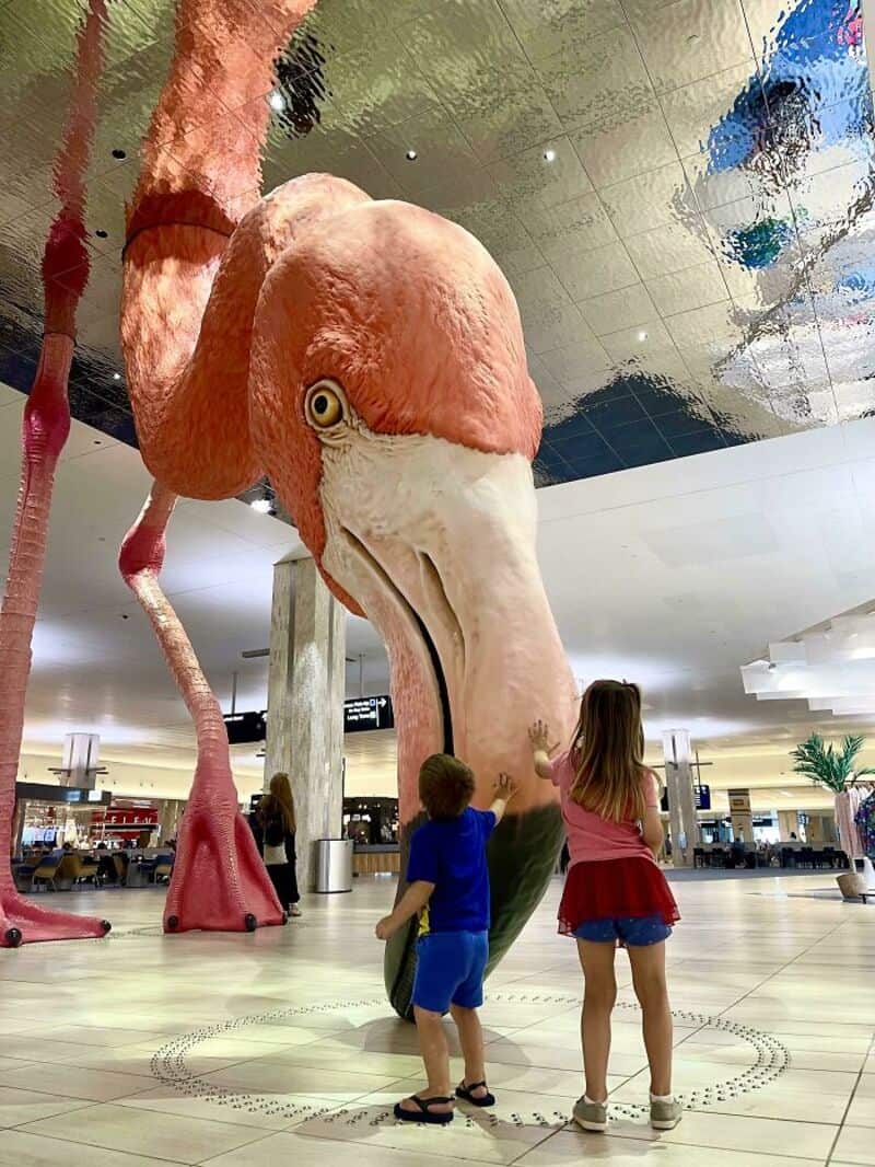 Large pink flamingo statue in a shopping mall with two children nearby.