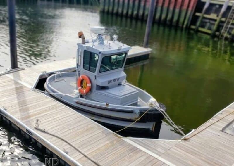 US Navy boat docked at a wooden pier on calm water.