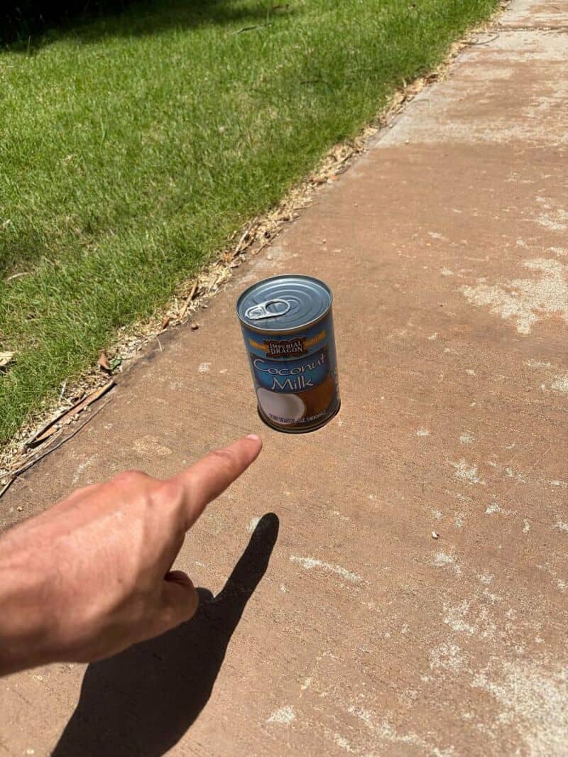 A can of sweetened condensed milk appears to float in midair on a sidewalk.