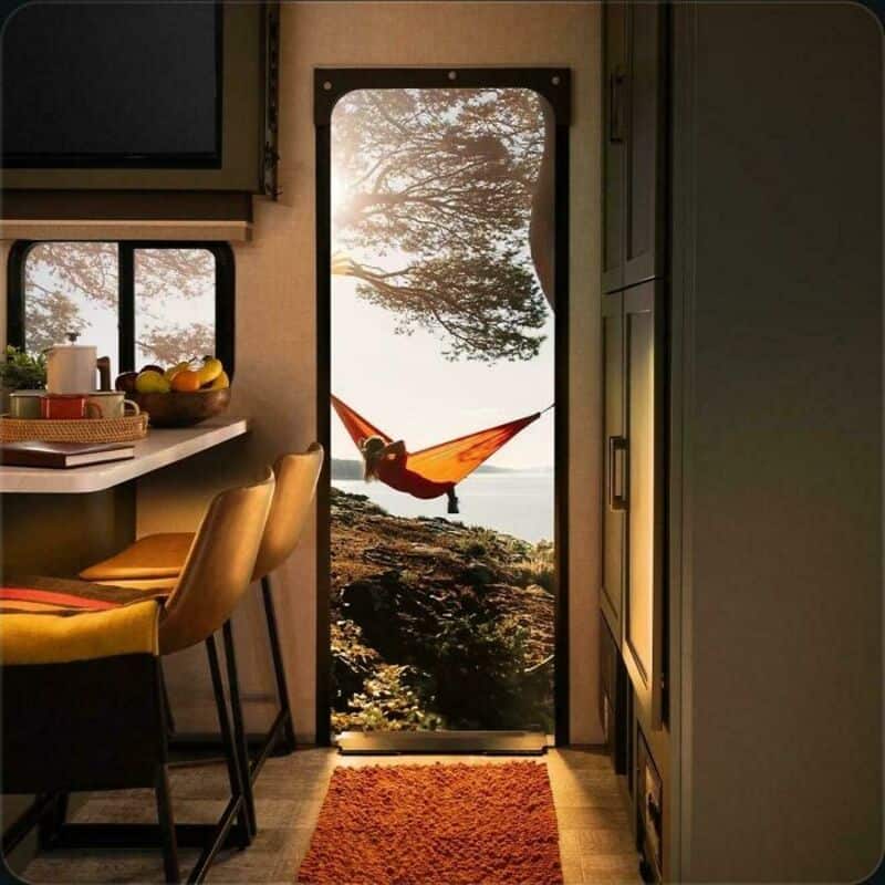 Person relaxing in hammock outside through door, with trees and water in background.