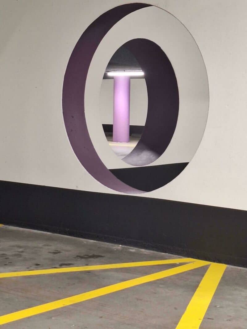 Modern parking garage with circular cutouts and purple lighting.