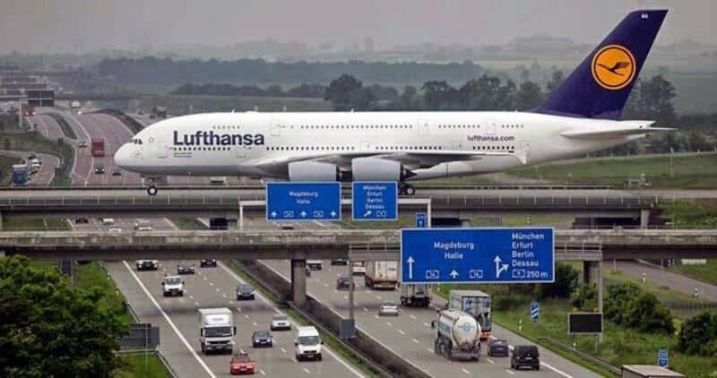 Lufthansa airplane flying low over highway with cars and road signs.