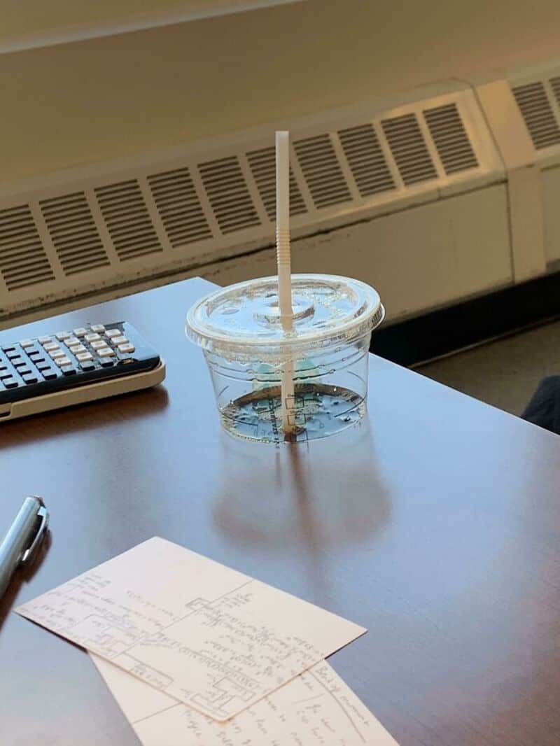 Empty plastic cup with straw on a desk, with papers and a calculator nearby.
