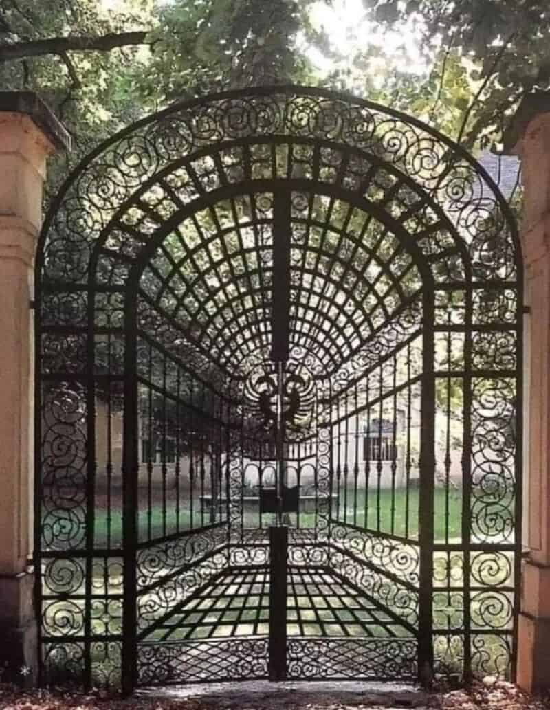 Ornate black wrought iron gate with intricate patterns, set between stone pillars.