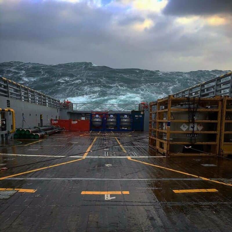 Stormy sea seen from a ship deck with containers and equipment.