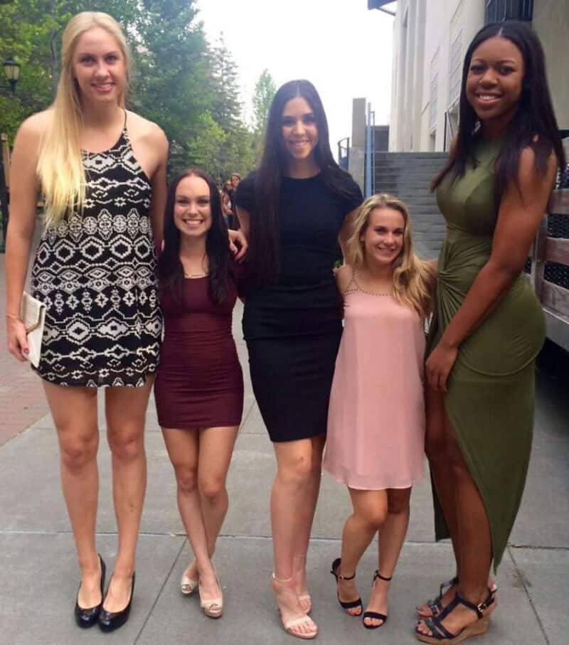Group of five women standing outdoors, smiling, in casual and semi-formal dresses.