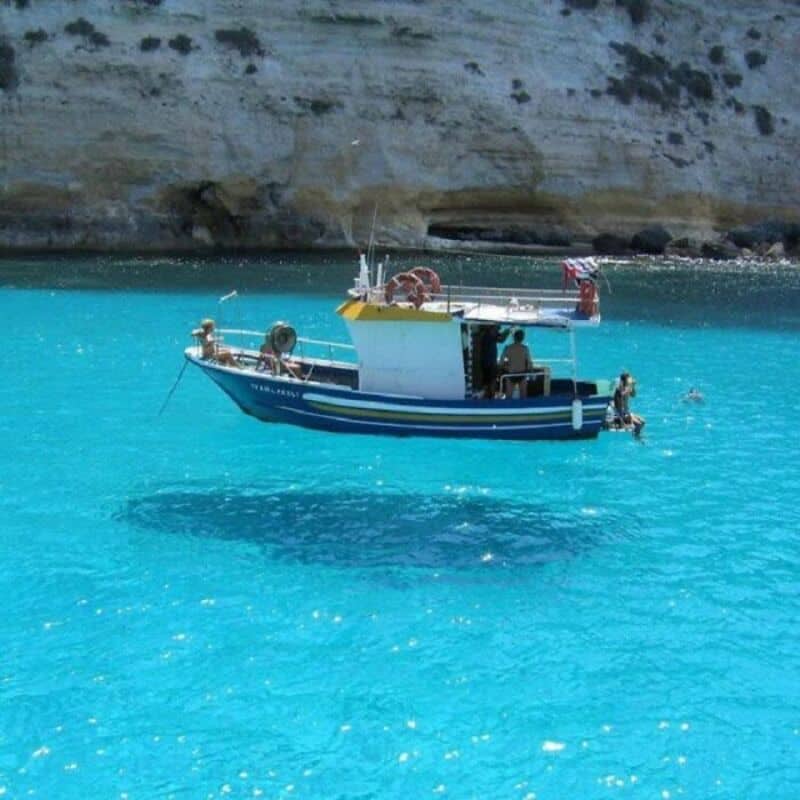 Boat floating on clear blue water near rocky shoreline.