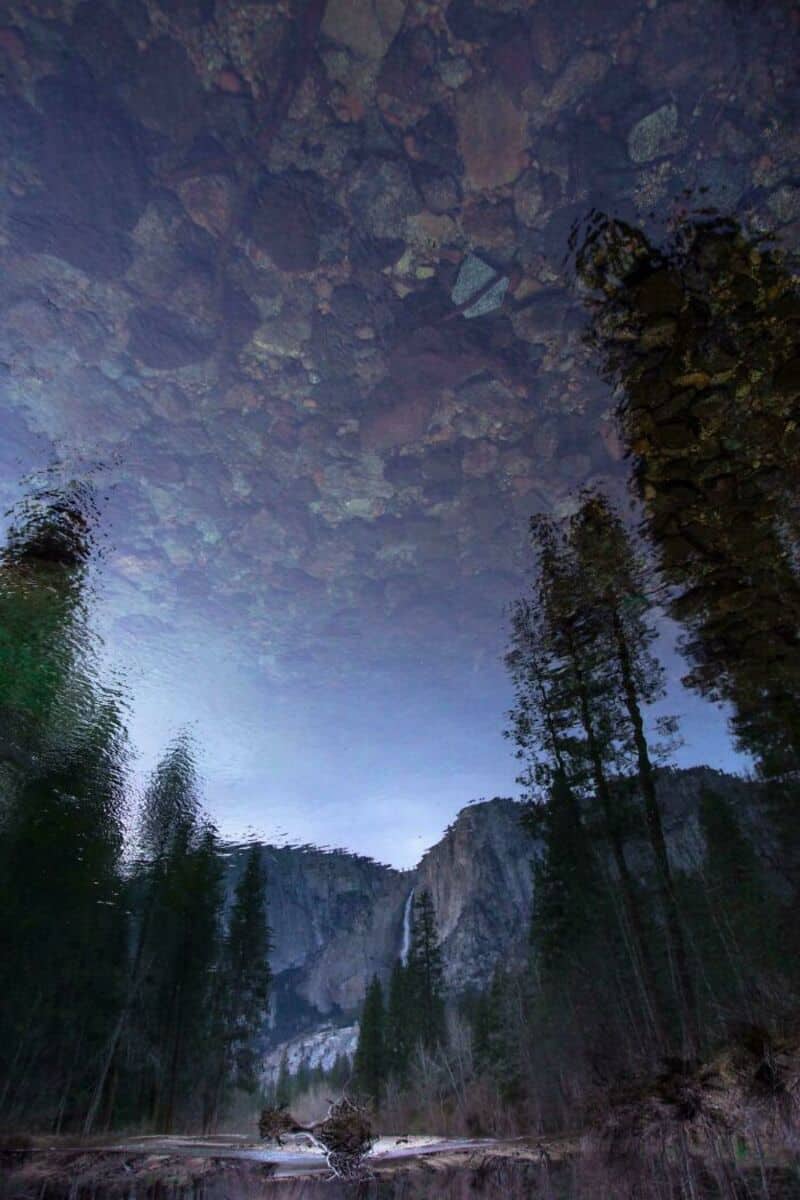 Reflection of trees and sky in a clear mountain lake with rocks above.
