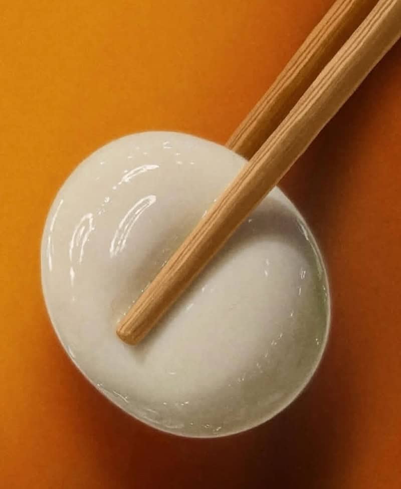 Chopsticks resting on a white ceramic bowl with a creamy substance, orange background.