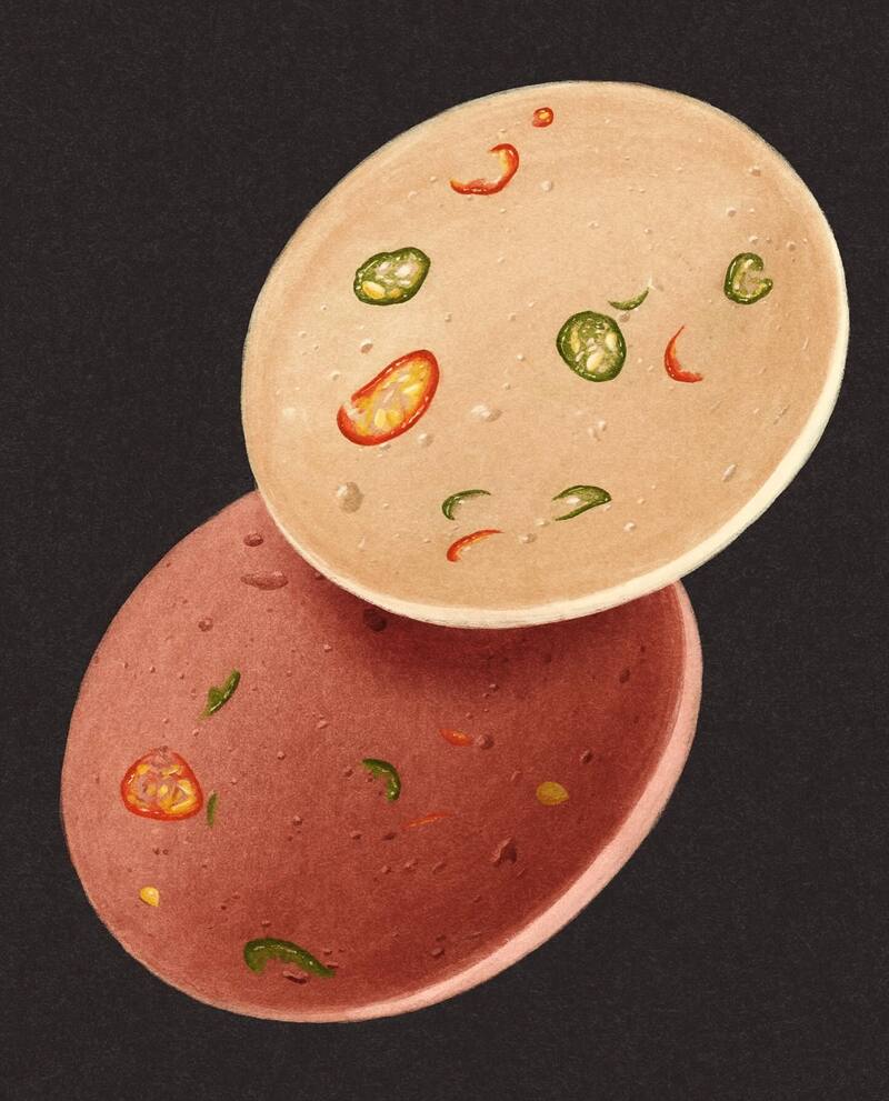 Two bowls of spicy soup with chili and herbs, one white and one pink, on a black background.