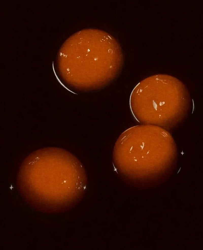 Four orange spheres floating in dark water with reflections and sparkles.