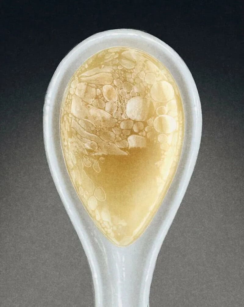 Close-up of a white spoon with a yellowish liquid and bubbles inside.