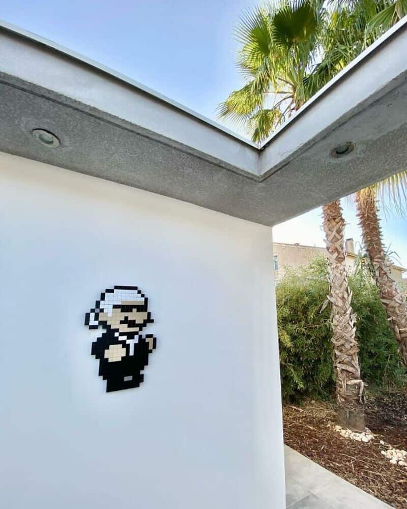 Pixel art of a character in a black suit and white hat on a white wall.