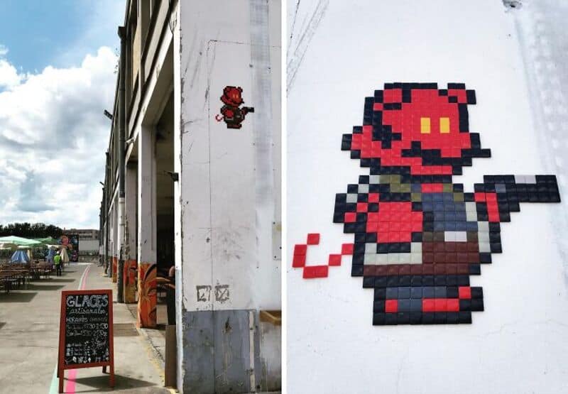 Pixel art of Mario and a red creature on a white wall in street art mosaic.