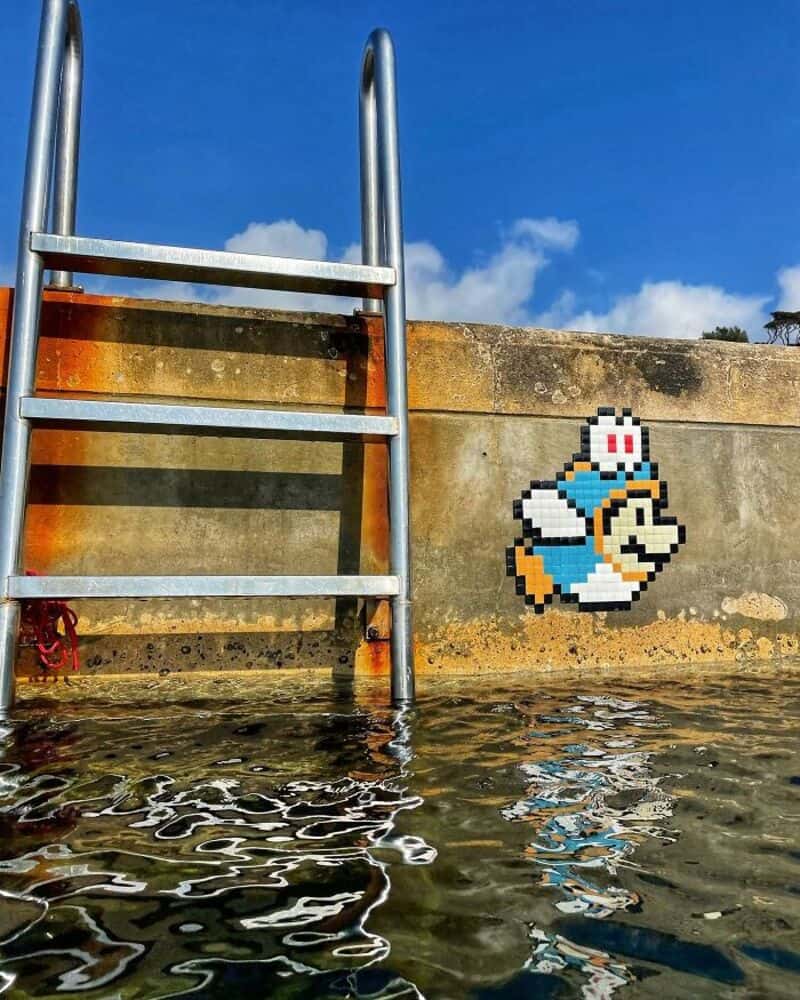 Pixel art of a character from Super Mario on a wall near water and a ladder.